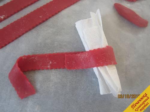 16) Раскатаем красный марципан. Нарежем несколько полосок нужной Вам длины, для банта и для обвязки. Обернём, как на фото, полоску вокруг сложенной салфетки.