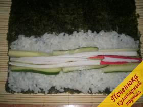 4) На васаби выложить порезанные крабовые палочки. С обеих сторон, как бы вкапывая в рис, выкладывается свежий огурчик, также порезанный тонкими длинными полосками. 