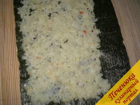 3) На лист нори выложить рис, оставив около 1,5 см незаполненным с одного края. Во время выкладывания крупы руки смачивать в воде с уксусным раствором. 